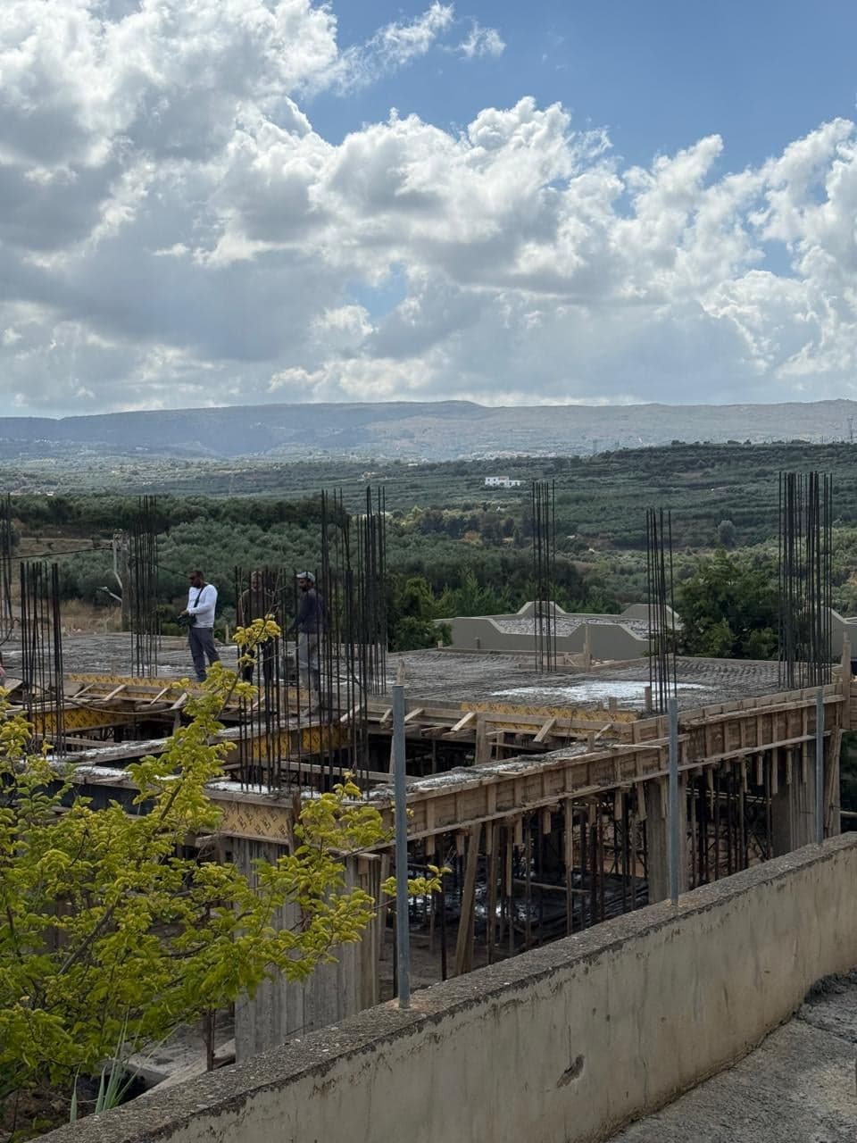 Bau von Creta Hills, Oktober 2026: Arbeiter auf der Obergeschossdecke, dahinter Olivenhaine und Hügel